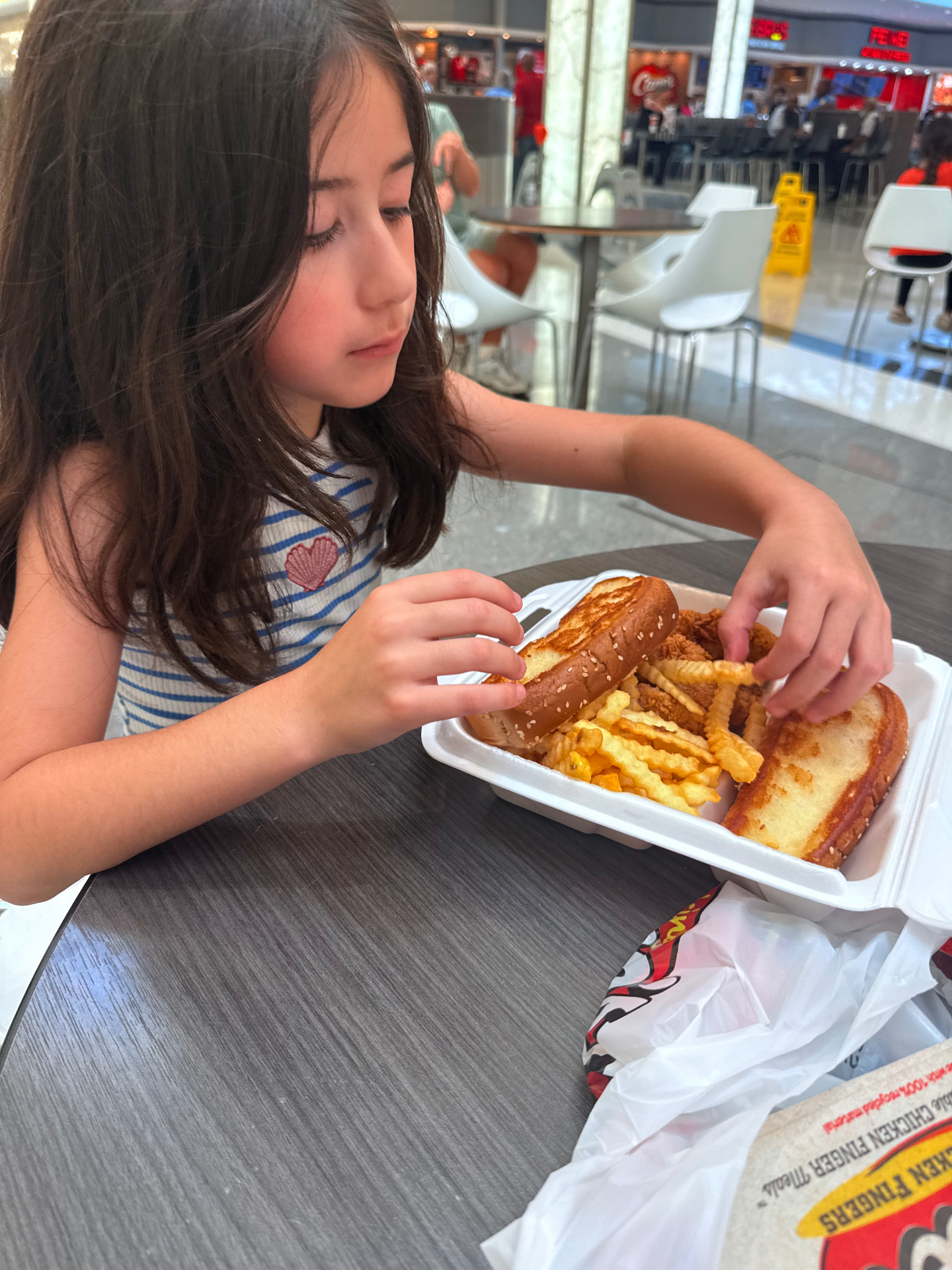 Mira taking a snack break with a Raising Cane's chicken sandwich and crinkle-cut fries at the mall food court between squishy store stops