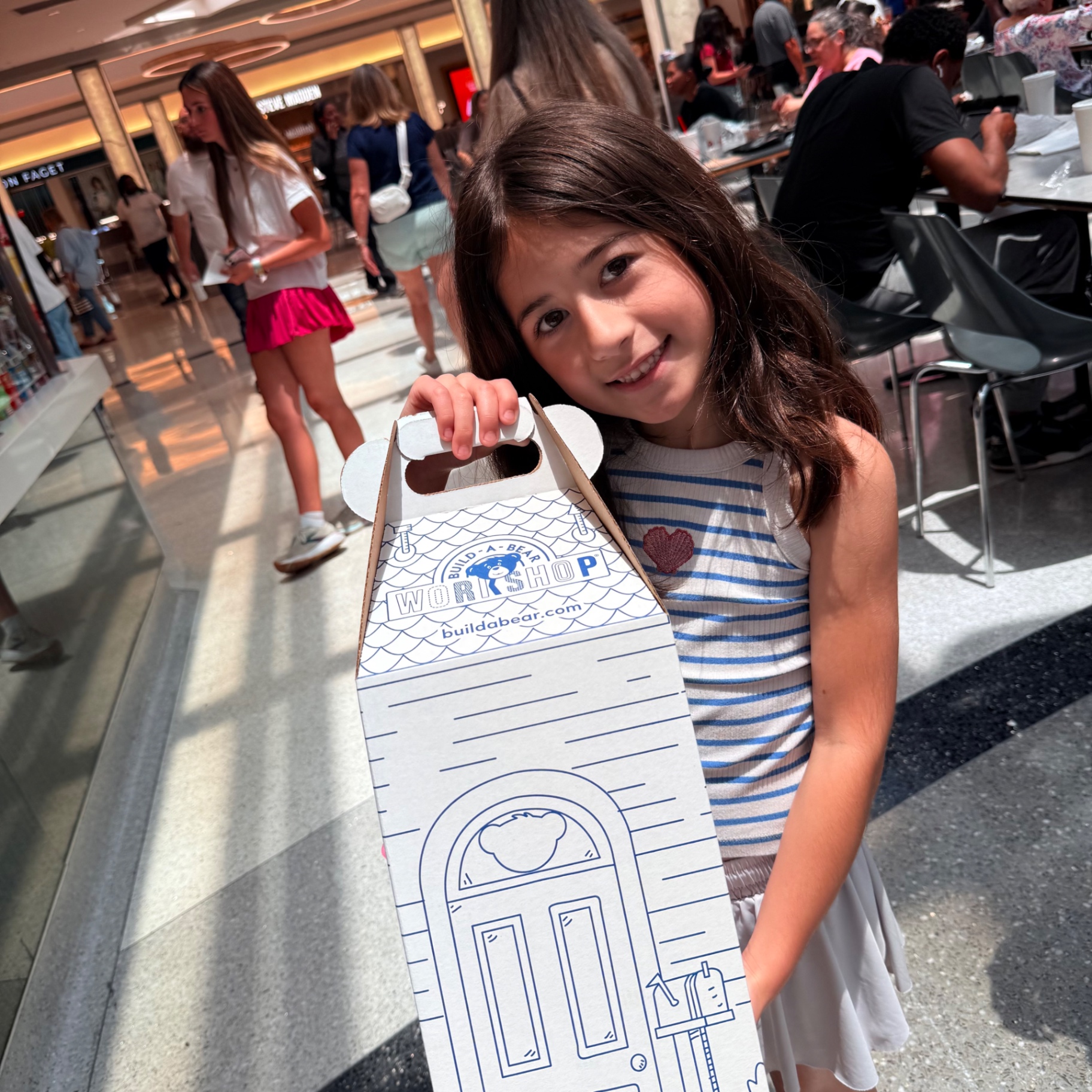 Mira smiling at the mall holding a white Build-A-Bear Workshop Cub Condo carry box with her brand-new plushie inside after a successful squishy hunt