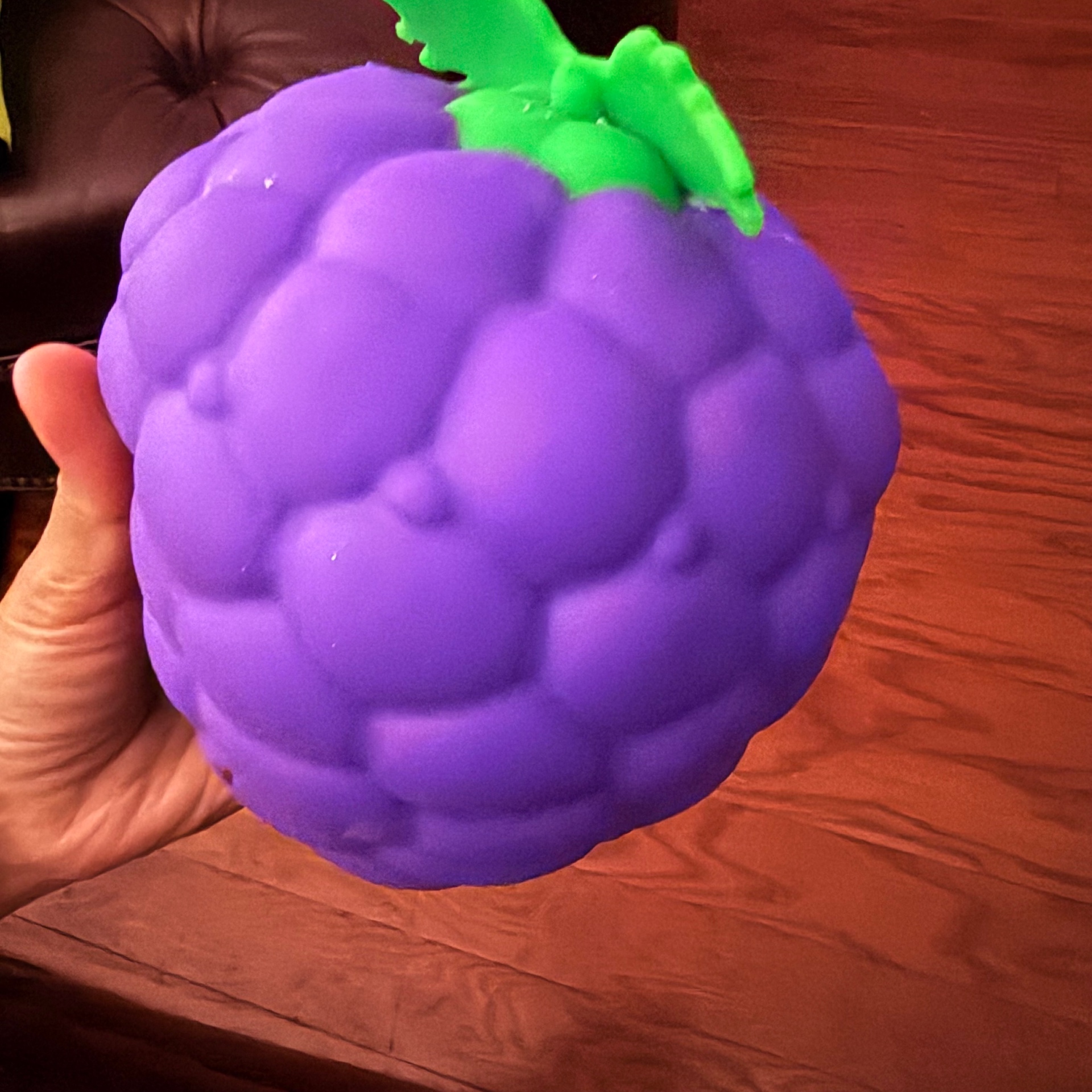 Kid's hand squeezing a giant purple grape-shaped slow-rise squishy toy with a bright green leafy stem — a Mira's Lemonade Squishy squishy review favorite